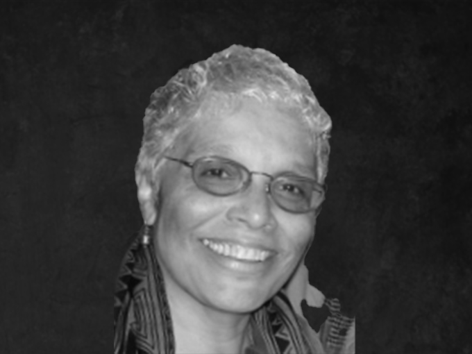 Pat smiling at the camera. She is wearing glasses in front of a photo backdrop.