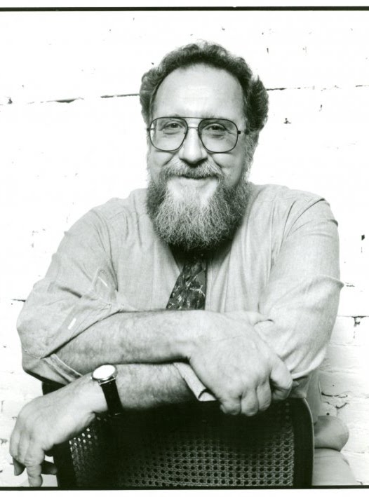 Ron Schiffman in grayscale smiling with arms crossed on a chair.