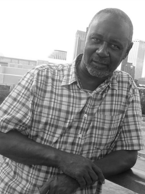 Rudy leaning on a rail in the city. He is wearing a flannel shirt.