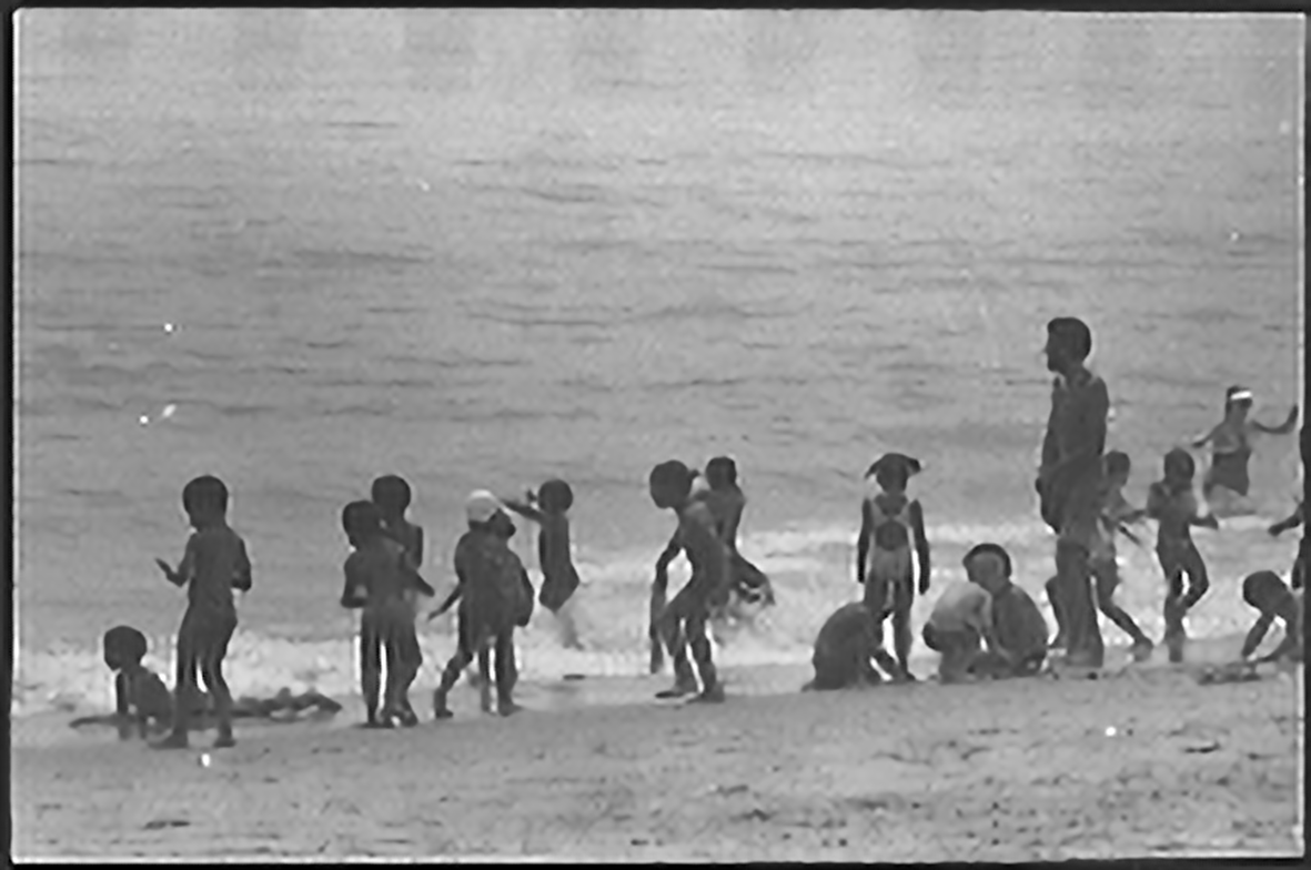 A silhouette of children playing on the beach at the surf.
