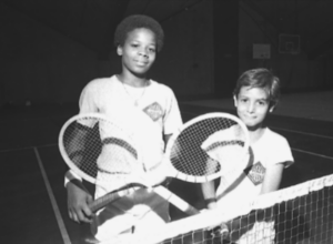 Two students crossing their tennis rackets in front of the net