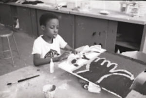 Student seated at a table with glue and a paint brush