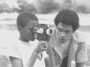 a student looking through a camera as a counselor offers assistance