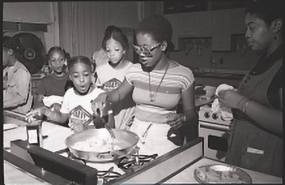 A counselor stirring food in a frying pan as a group of students look on.