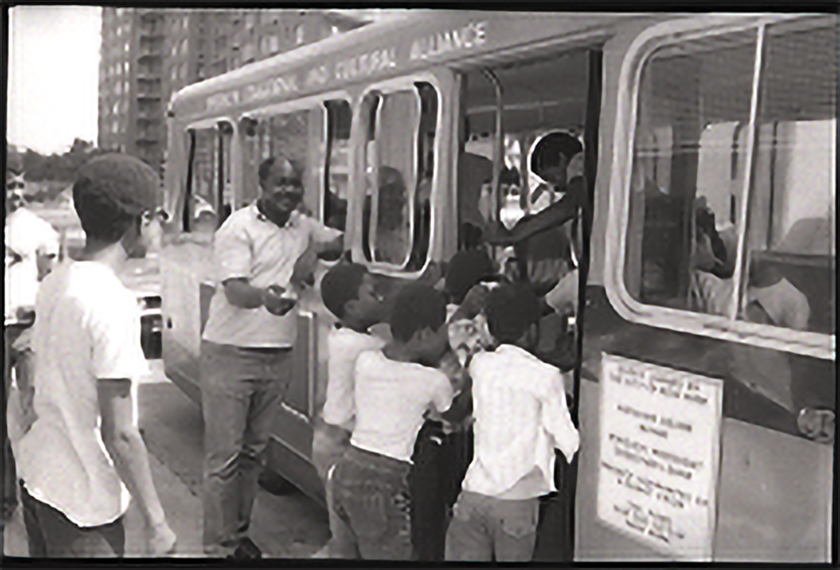 Students filing into a bus. A counselor waves them in.
