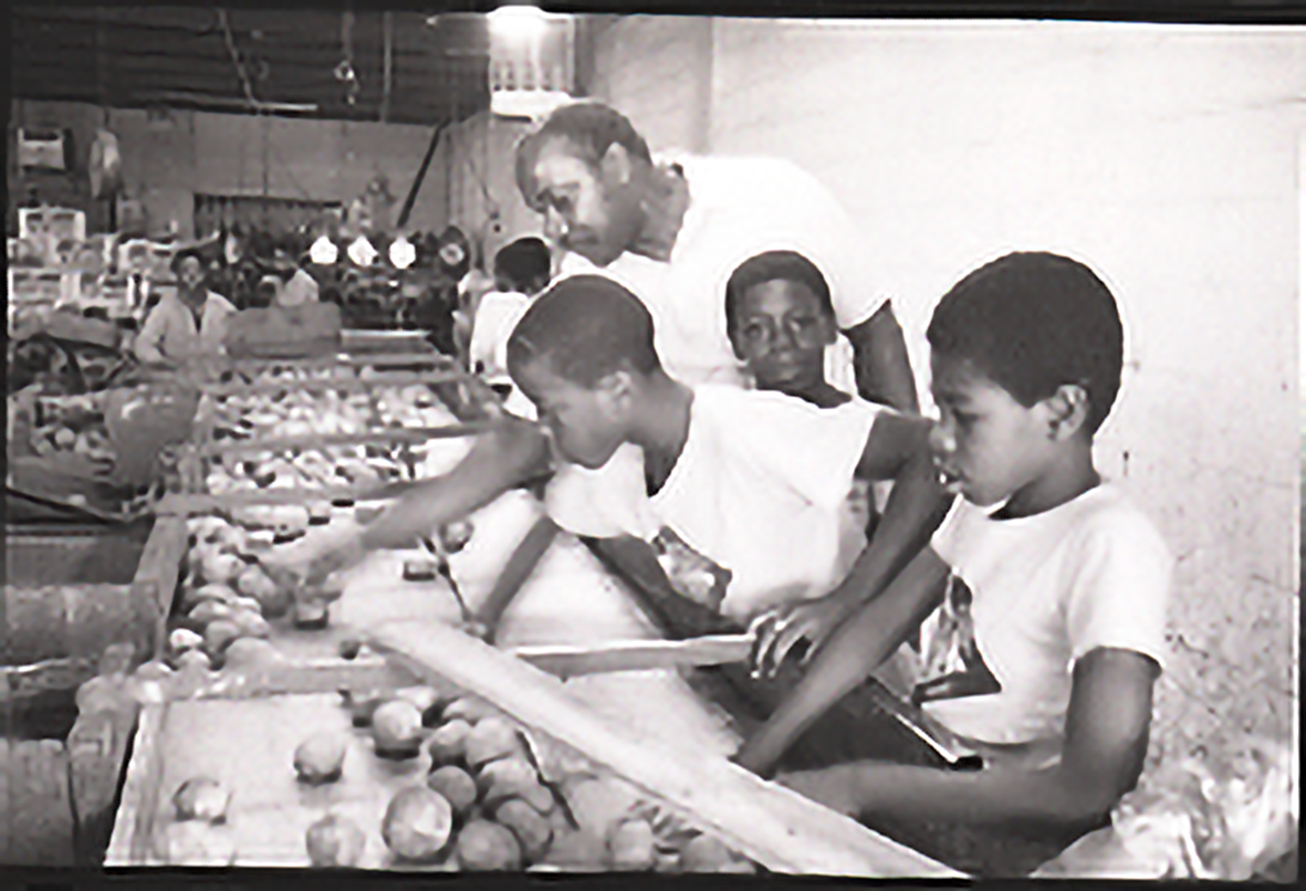 Students in front a produce sorting machine. A counselor points at the sorting mechanism.