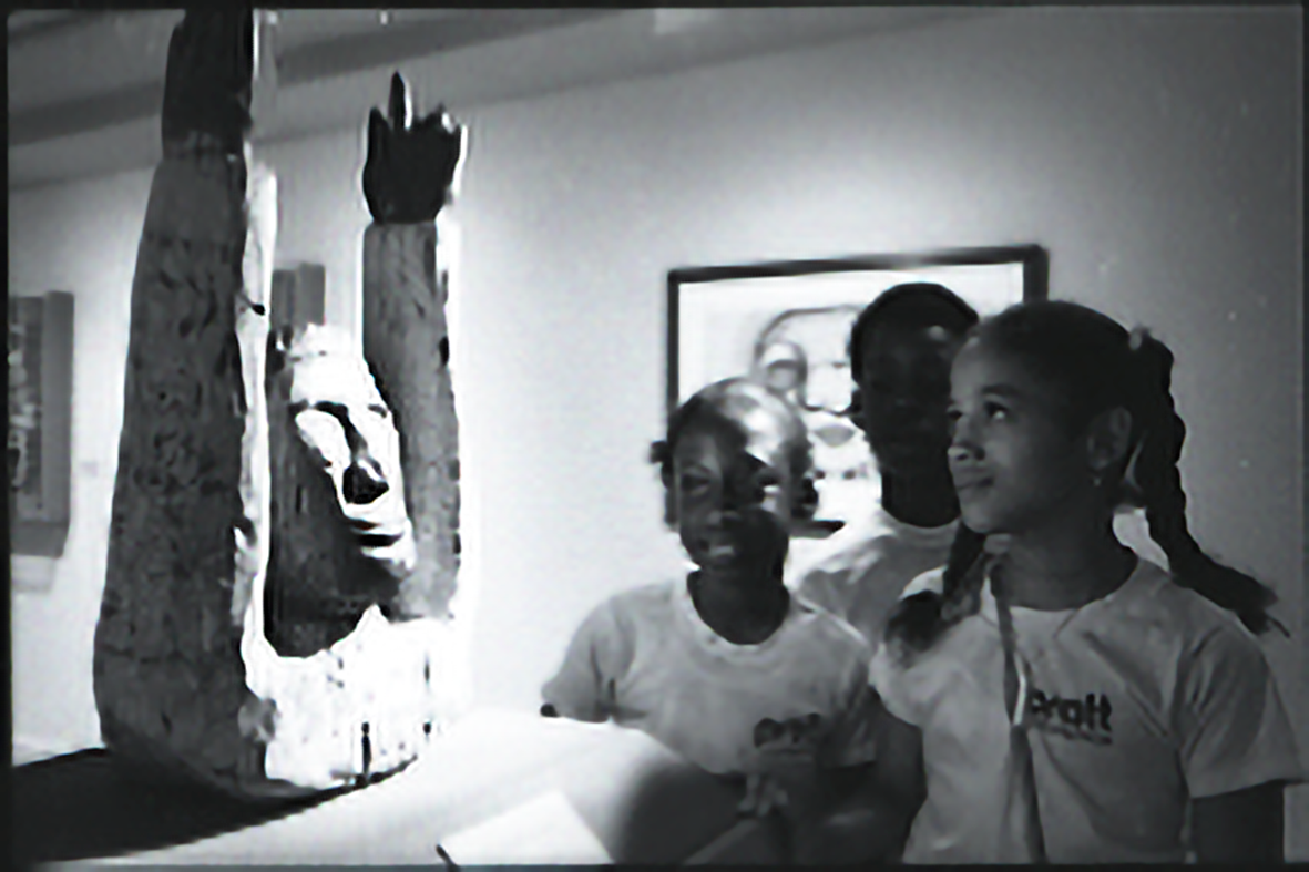 Three students looking at a sculpture of a torso with arms outstretched