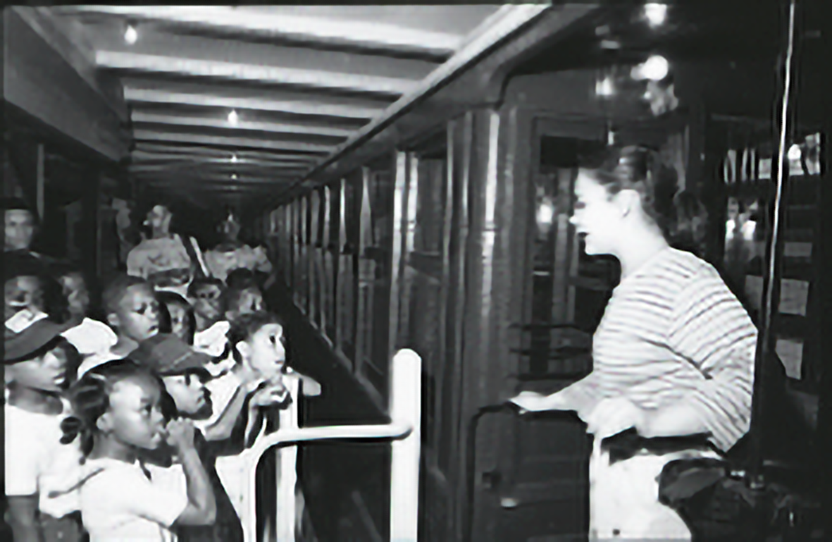 A counselor stands at the entrance of the Transit Museum. A group of students are lined up in front.