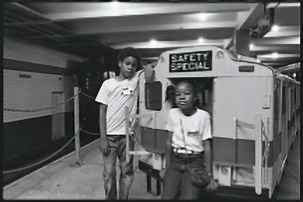 A student sitting on a model subway car labeled "Safety Special" Another student leans on the car.