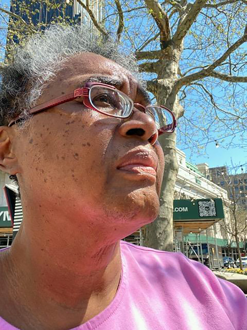 Adrienne Gantt staring away from the camera. She is wearing a pink shirt and red glasses.